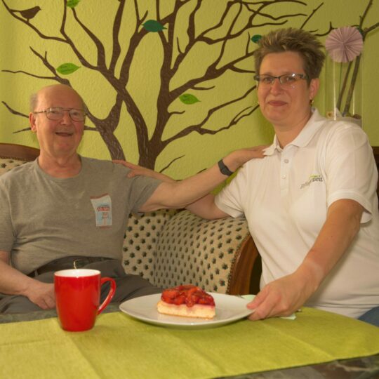 Ein Mann und eine Pflegerin am Tisch mit Kaffee und Kuchen